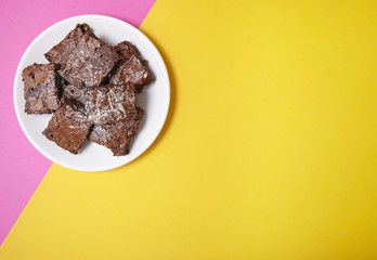A plate of freshly baked chocolate fudge brownies on a bright pink and yellow background, with blank space at side