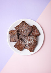 A plate of freshly baked chocolate fudge brownies on a pastel pink and purple background