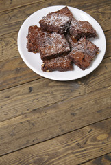 A plate of freshly baked chocolate fudge brownies on a rustic wooden table background with blank space below