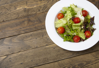 A bowl of fresh garden salad on a rustic wooden dining table background with empty space at side