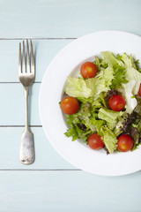 Aerial view of a dish of classic side salad with fork, on a blue wooden table top background
