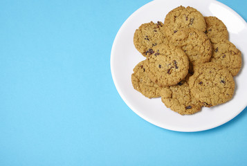 A plate full of freshly baked oatmeal and raisin cookies on a bright blue background with blank space at side