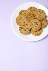 A plate full of freshly baked oatmeal and raisin cookies on a pastel purple background with blank space below