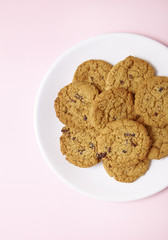 A plate of freshly baked oatmeal raisin cookies on a pastel pink background
