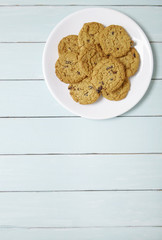 Aerial view of a plate full of freshly baked oatmeal and raisin cookies on a blue wooden table background with blank space below