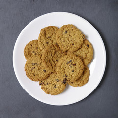 Overhead view of a plate full of freshly baked oatmeal and raisin cookies on a dark slate background