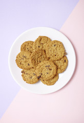 Overhead view of a plate full of freshly baked oatmeal and raisin cookies on a pastel pink and purple background
