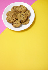 A plate full of freshly baked oatmeal and raisin cookies on a bright pink and yellow background with blank space below