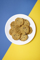 Overhead view of a plate full of freshly baked oatmeal and raisin cookies on a blue and yellow background