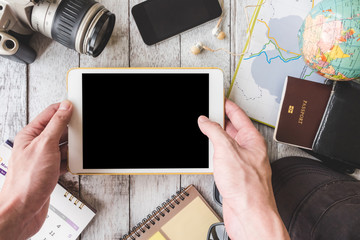 Top view of Male hands holding tablet with travel equipment on table