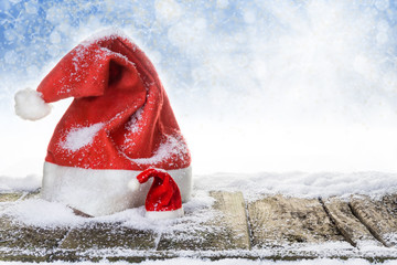 Weihnachtsmützen auf verschneitem Holzboden vor blauem Hintergrund mit Bokeh und Sternen