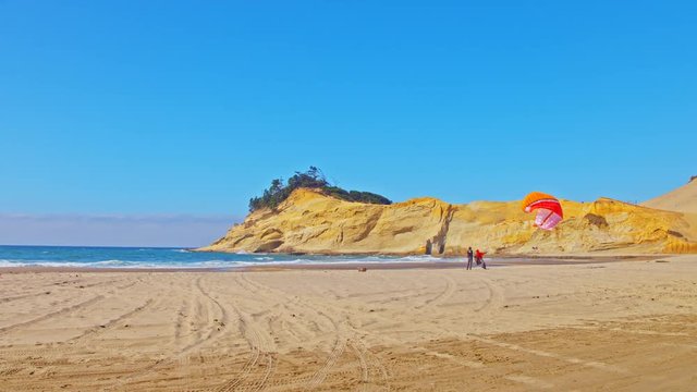 Instructor giving paragliding lesson to a student on a Pacific ocean beach on a sunny day by Cape Kiwanda in Oregon, cinematic, smooth, sliding, panning camera shot