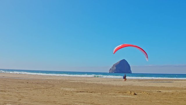 Man practicing his paragliding skills on a Pacific ocean beach on a sunny day by Cape Kiwanda in Oregon, cinematic, smooth, sliding, panning camera shot