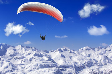 Paragliding over the mountains on background of blue sky and whi