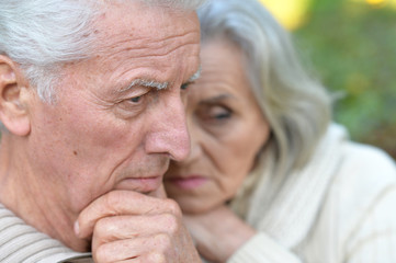 Sad elderly couple standing embracing outdoors