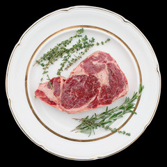 Raw rib-eye steak on plate, isolated