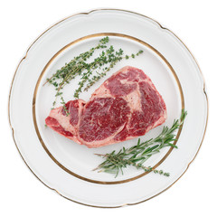 Raw rib-eye steak on plate, isolated