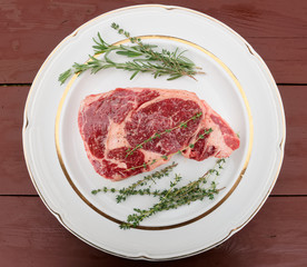 Raw rib-eye steak on plate, wooden table