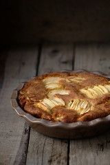 Rustic french apple cake with vanilla and rum in a round ceramic baking pan. Wooden background.