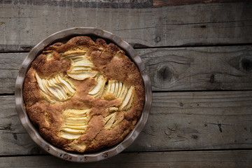 Rustic french apple pie with vanilla and rum in a round ceramic baking pan. Wooden background. Horizontal.