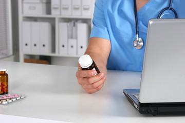 Close-up view of female doctor hand holding bottle with pills and writing prescription. Healthcare,...