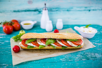 Delicious sandwich with caprese salad with ripe tomatoes and mozzarella cheese with fresh basil leaves. Italian food. 