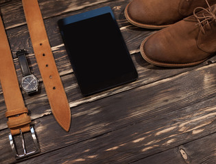 Men's brown clothing and accessories set: boots, leather belt, watch and pc-tablet
on wooden background. Casual stile set, hipster style, businessman