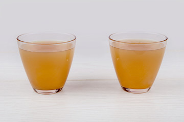 Two glasses of juice on white wooden background.