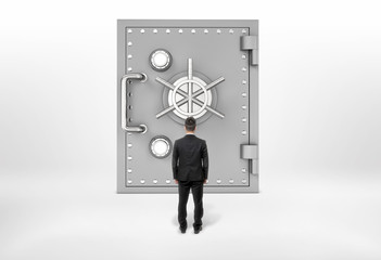 Businessman standing back to us looking at the giant safe door, all isolated on the grey background.