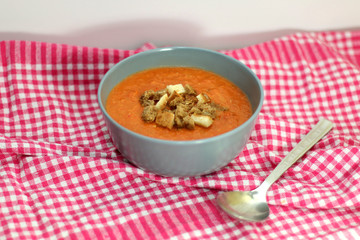 Gazpacho in a bowl with bread pieces on red checkered napkin. Selective focus. 