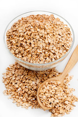 Uncooked oatmeal in glass bowl and spoon on white background. Healthy food. Close up, high resolution product.