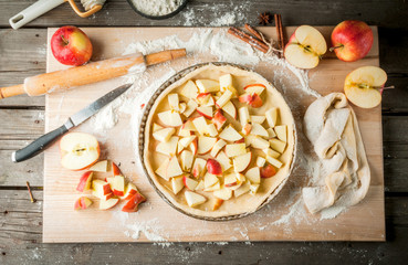 Cooking apple pie, kitchen wooden table, the girl (his hands in the frame) lays out the dough and apples into a form, top view