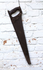 Aged wood saw hanging on white brick wall background. Black handlesaw carpentry equipment.