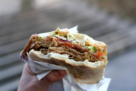 Doner kebab stuffed into a pita with tomatoes, cabbage and lettuce. Eating outdoor. Selective focus. 
