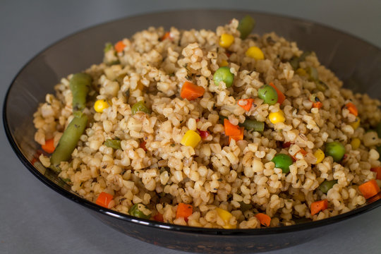 Bulgur with different vegetables, dried herb and soy sauce in a bowl on gray kitchen table.