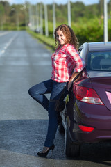 Young woman in red plaid shirt and on high heel posing near car on the highway, full length