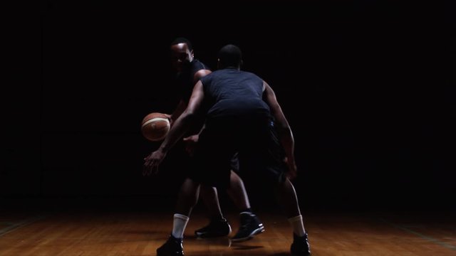 A basketball player challenges a defender and tries to dribble the ball past him