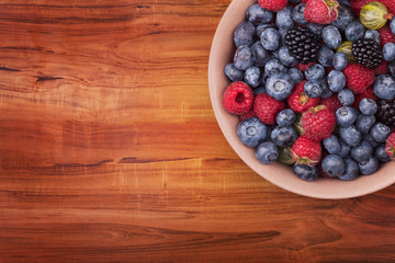 Brown ceramic plate with berries on the right top corner of the wooden table with clipping path. Top view.