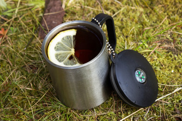 Metal travel mug of tea with lemon on grass outdoors