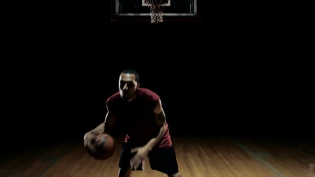 A solo basketball player does some dribbling moves in front of the camera