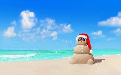 Fototapeta na wymiar Sandy snowman in Christmas Santa hat and sunglasses at beach