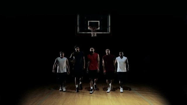 A group of basketball players walk, and pose for the camera in a line