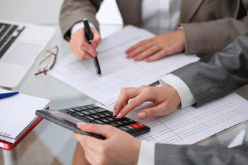 Two female accountants counting on calculator income for tax form completion hands closeup....