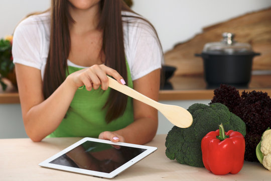 Young woman is going to cook healthy meal from vegetables. Close up of housewife with wooden spoon pointing into pepper and brocolli. Vegetarian concept.