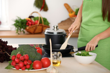 Fresh vegetables, salad and vegetable oil at the background of  woman is cooking by the stove in the kitchen
