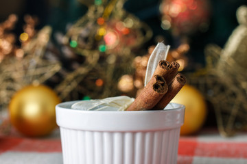 Cinnamon sticks on a white plate on a checkered tablecloth on the background of Christmas tree. Concepts of the New Year holiday. For holiday.
