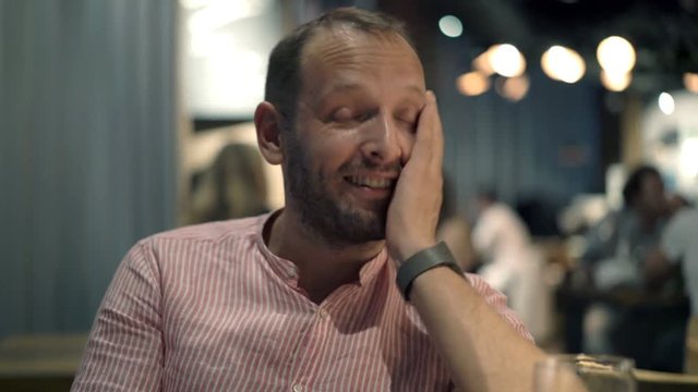 Portrait of happy, funny man talking to camera in cafe at night
