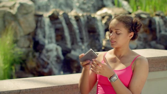 Young woman taking selfie and watch photo on smartphone. African girl making selfie portrait near waterfall. Female tourist taking selfie on beautiful nature background. Tourist selfie