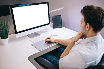 Young worker sitting in an office at the computer. Freelancer in a blue shirt. The designer sits in front of window in the workplace.