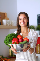 Smiling young woman holding vegetables standing in kitchen